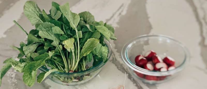 Radish greens in a glass bowl next to whole radishes in another bowl